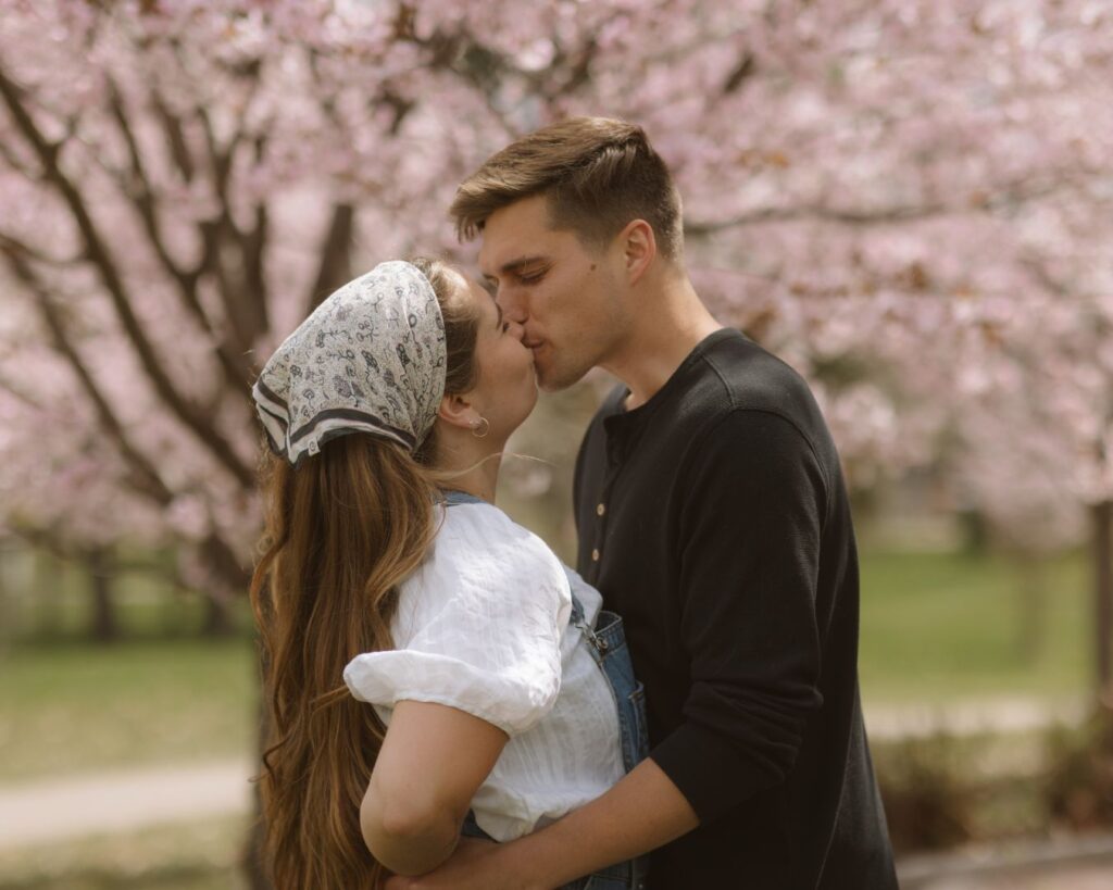 A couple kissing in front of fully bloomed cherry blossom trees at Como Park in the spring. 