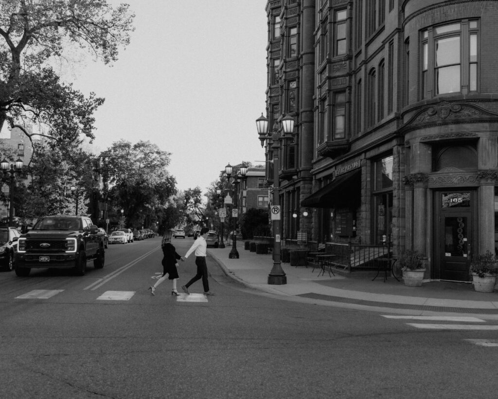 Black and white image of a couple holding hands and walking across a cross walk outside Nina's Cafe in St. Paul. 