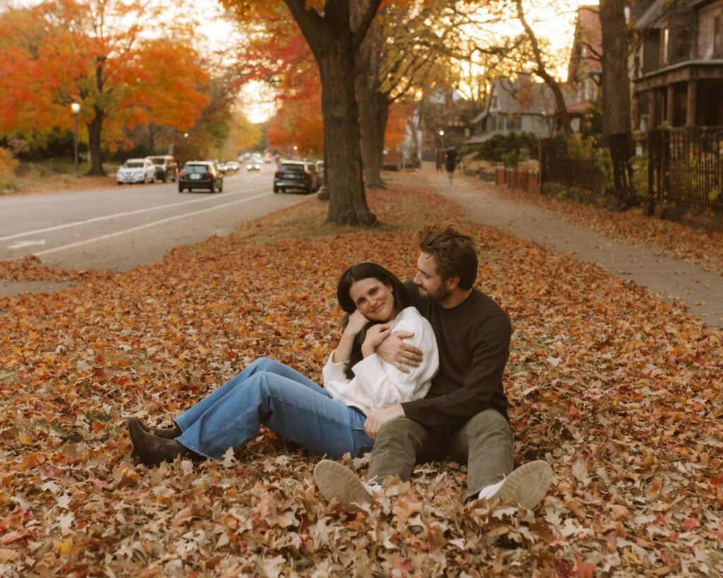 Couple sitting snuggled up in the orange fall leaves that have fallen to the ground on Summit Ave in St. Paul. 